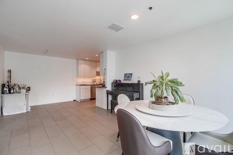 A white dining table with a potted plant on it and a kitchen in the background.