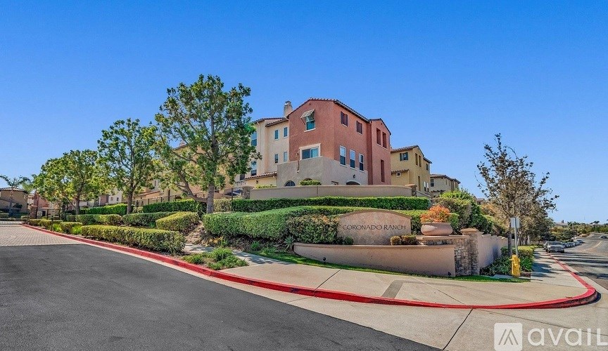 A street view of a residential area with a house named "CORONADO" and a clear blue sky.