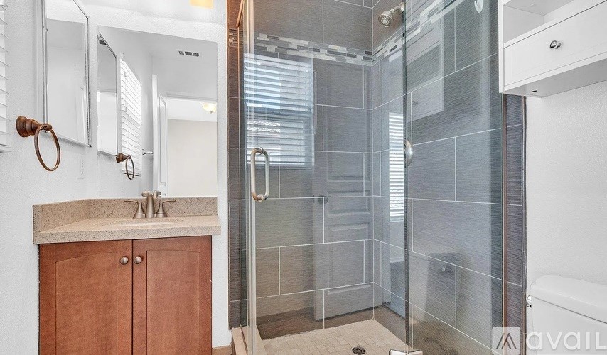 A bathroom with a glass shower stall and a sink with a wooden cabinet.