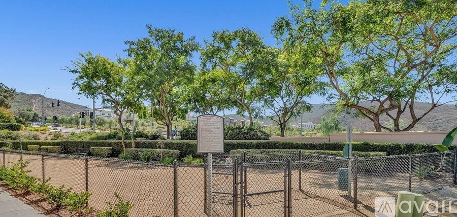 A chain link fence with a sign on it in front of a green hedge.