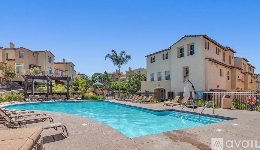 A swimming pool surrounded by lounge chairs and umbrellas in a sunny outdoor setting.