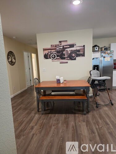 A room with a wooden floor and a wall with a picture of a car and a clock on the wall.