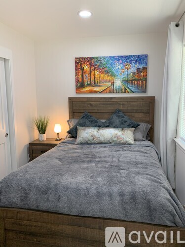 A bedroom with a bed, a nightstand with a plant, and a painting on the wall.