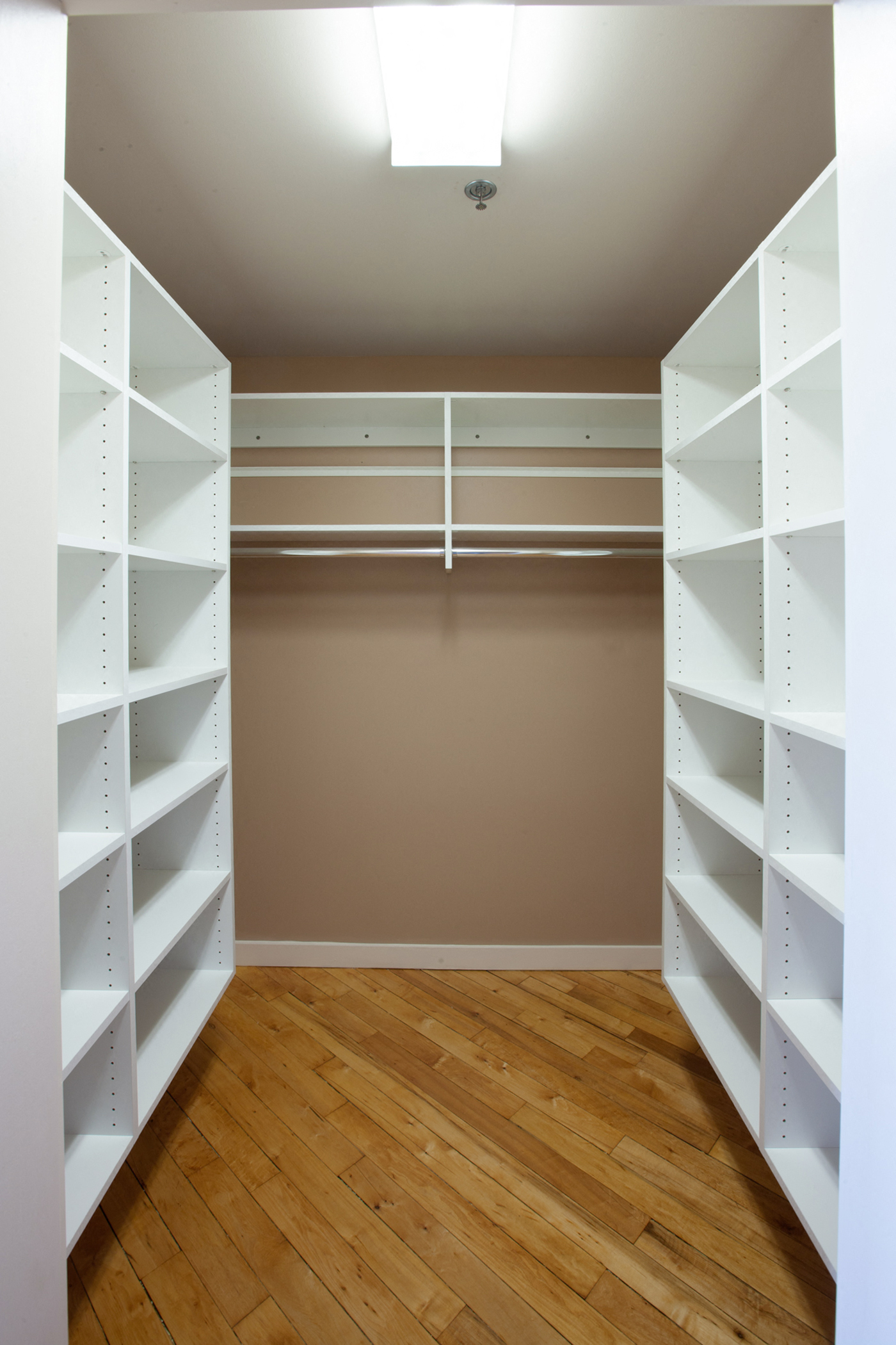 a walk in closet with white shelves and a wood floor
