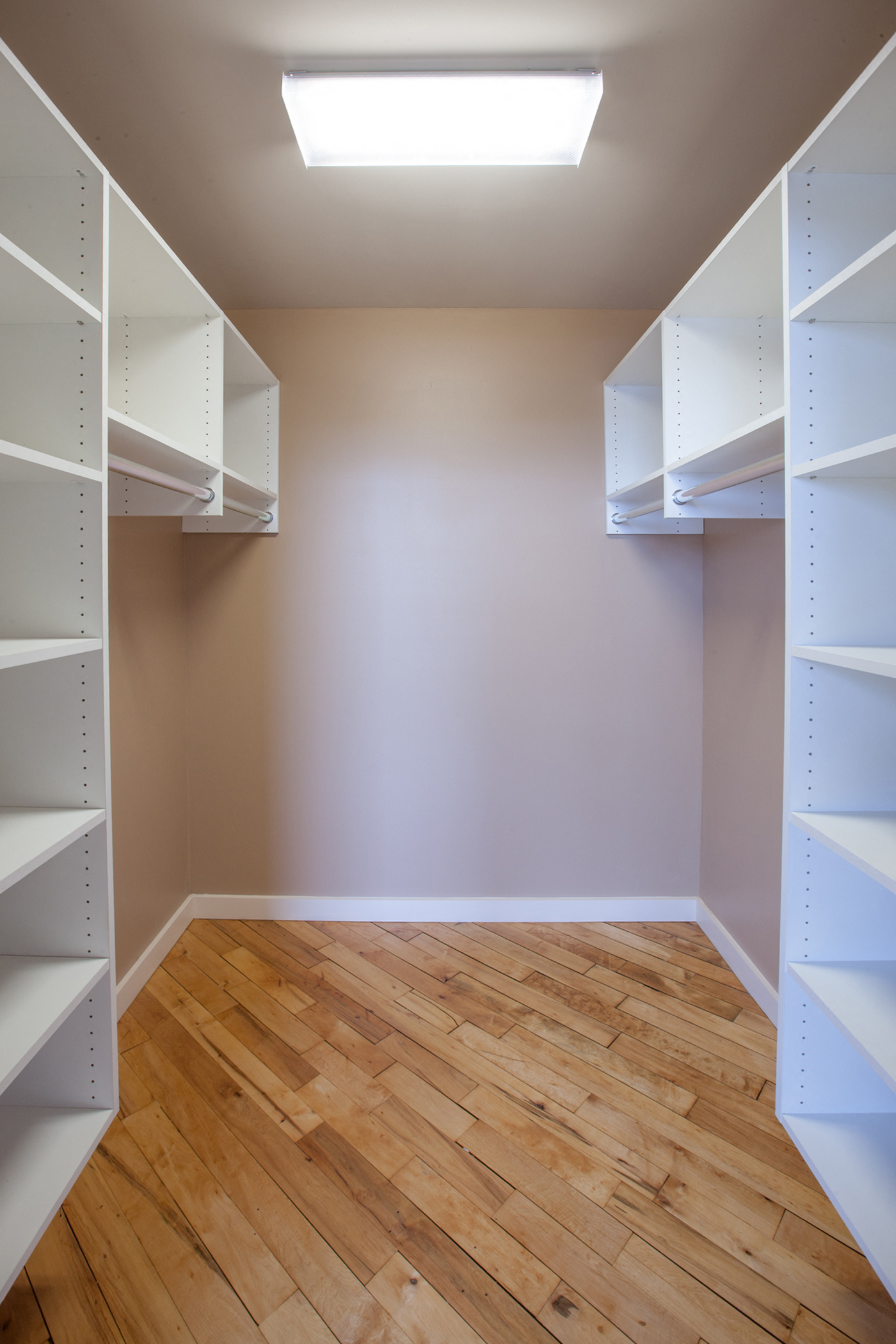 a walk in closet with white shelves and a wood floor