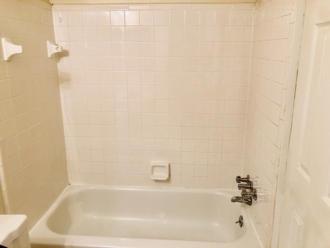 A white bathroom with a white tub and white tiles.