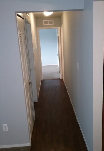 A hallway with a door on the left and a doorway in the distance.