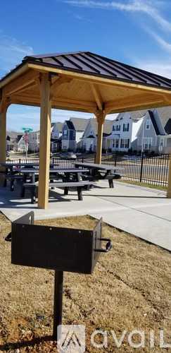 A wooden pavilion with a black roof is situated in a grassy area with a sign in front of it.