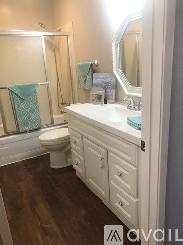 A bathroom with a white toilet, sink, and wooden floors.