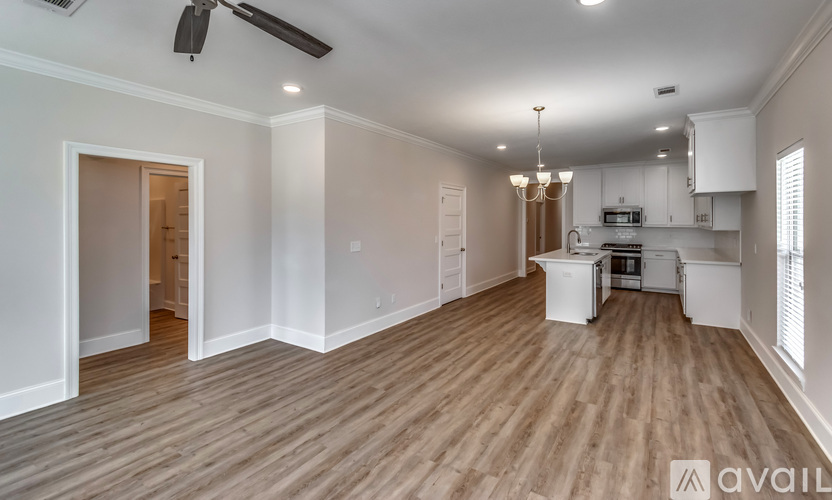 A spacious room with wooden flooring and a kitchen area in the background.