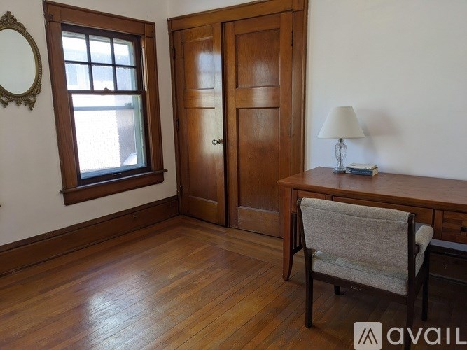 A room with a wooden floor, a wooden door, a wooden table with a lamp and a chair.