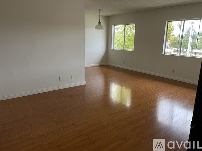 A room with wooden flooring and two windows.