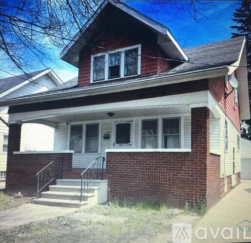 A red brick house with a white porch and a black metal railing.
