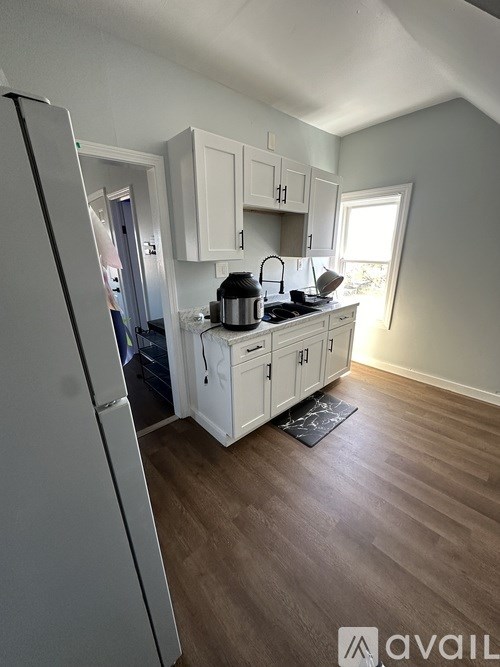 A kitchen with a white fridge, white cabinets, and a black mat on the floor.