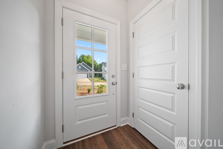 A white door with a glass window showing a view of a house and trees.