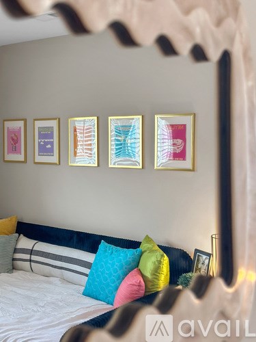 A bed with a white comforter and a blue pillow is in front of a wall with four framed pictures.