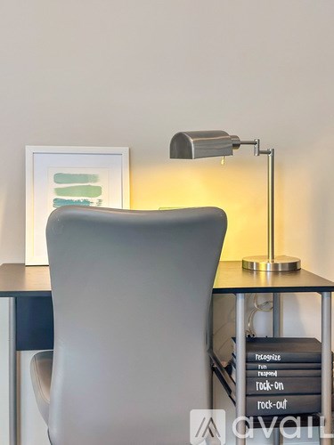 A white chair is in front of a desk with a lamp and a picture on the wall.