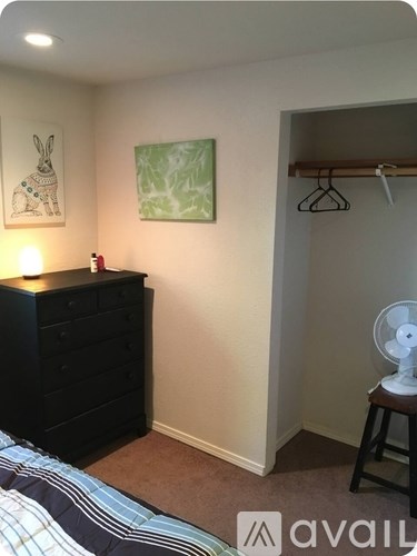 A room with a bed, a dresser, a painting, and a fan.