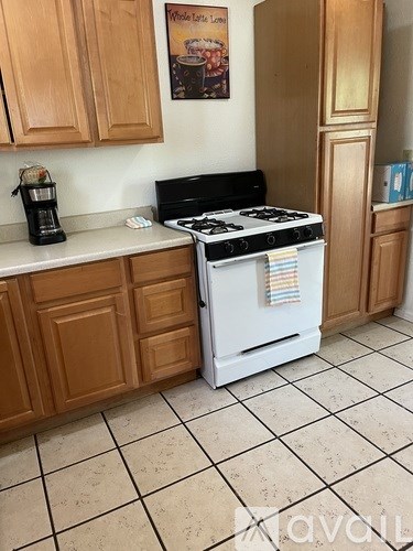 A white stove with a black top is in a kitchen with wooden cabinets.