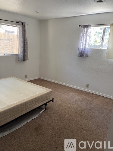 A bedroom with a bed, carpeted floor, and two windows.