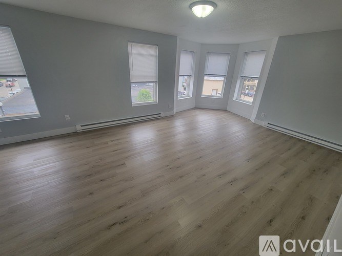 A spacious room with wooden flooring and large windows.