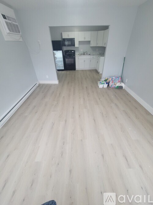 A room with light wood flooring and a kitchen in the background.