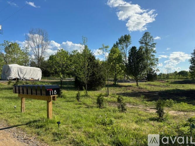 A sign with the number 118 is in the foreground of a grassy field with trees and a clear sky.