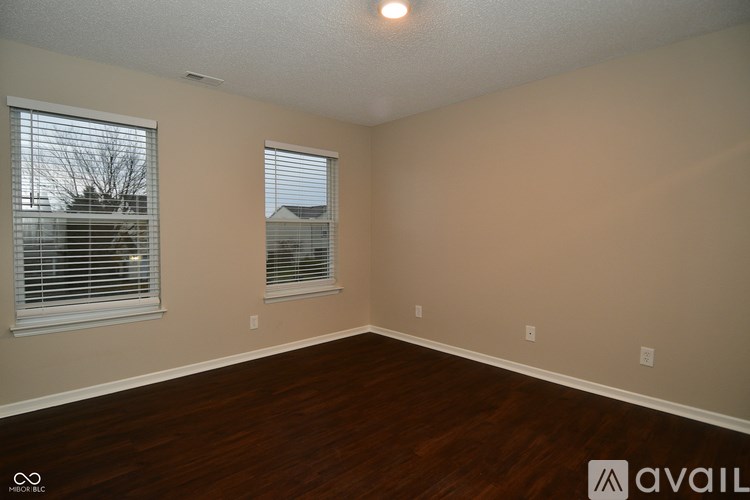 A room with wooden floors and two windows with blinds.