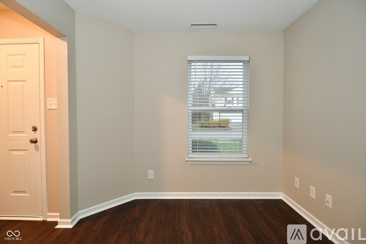 A room with a white door, a window with blinds, and a wooden floor.