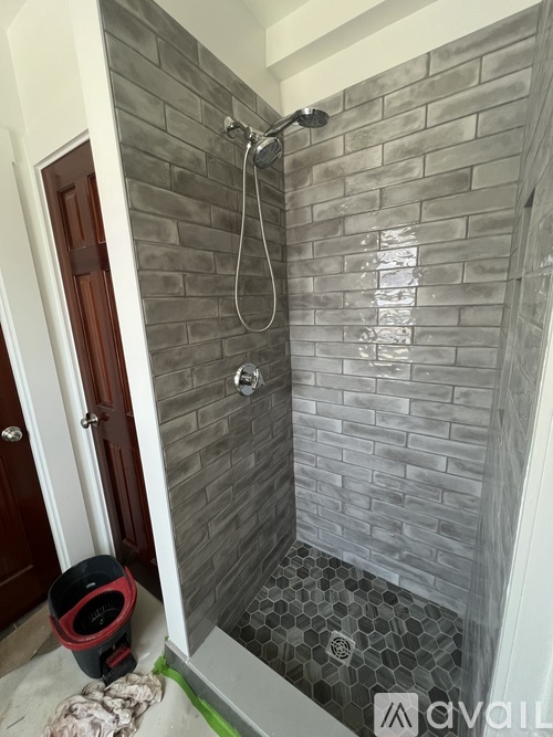 A bathroom with a grey tiled shower and a red vacuum cleaner.