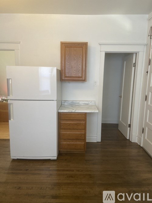 A white refrigerator stands in a kitchen with wood floors and white walls.