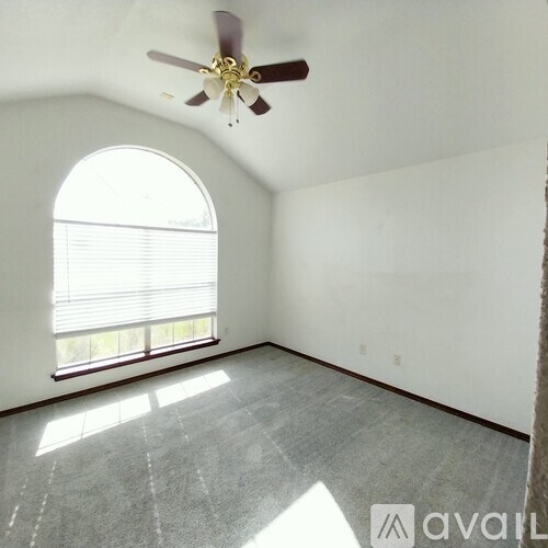 A room with a ceiling fan and a large arched window.