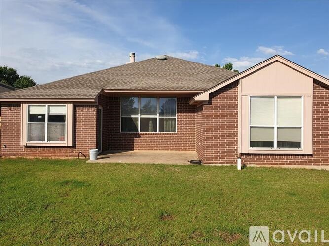 A house with a brown roof and brick walls is surrounded by a grassy lawn.