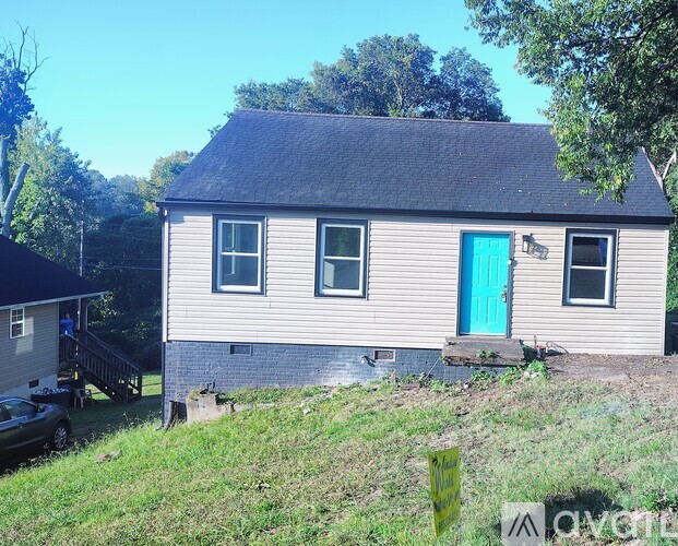 A small house with a blue door is surrounded by greenery.