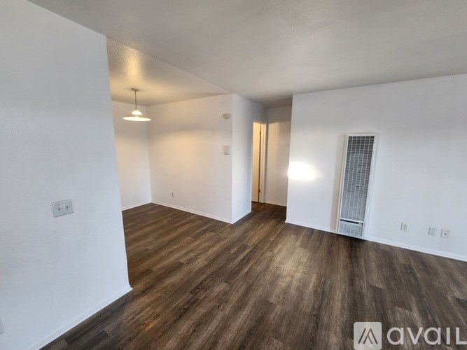 A room with wooden flooring and white walls, with a door on the right and a window on the left.