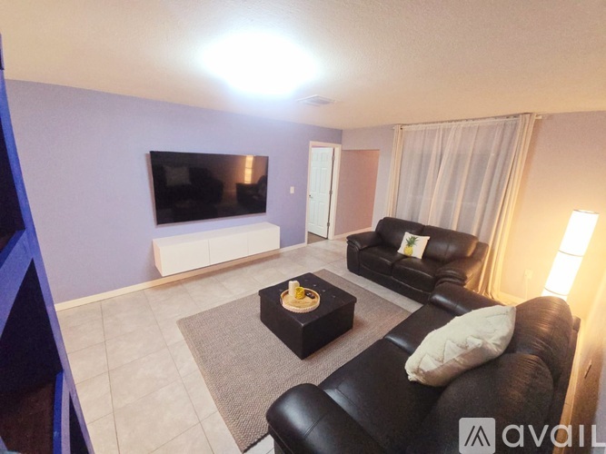 A living room with a black leather couch and a flat screen TV mounted on the wall.