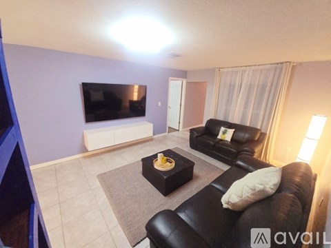 A living room with a black leather couch and a flat screen TV mounted on the wall.