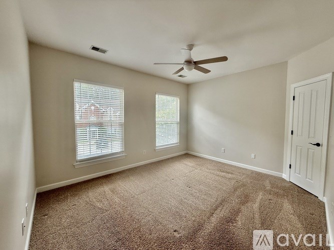 A room with a carpeted floor, a ceiling fan, and a window with blinds.
