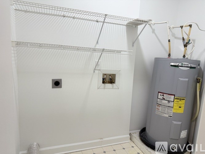 A room with a grey water heater and a white wall.