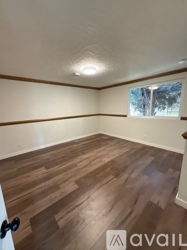 A room with wooden flooring and a window showing trees outside.