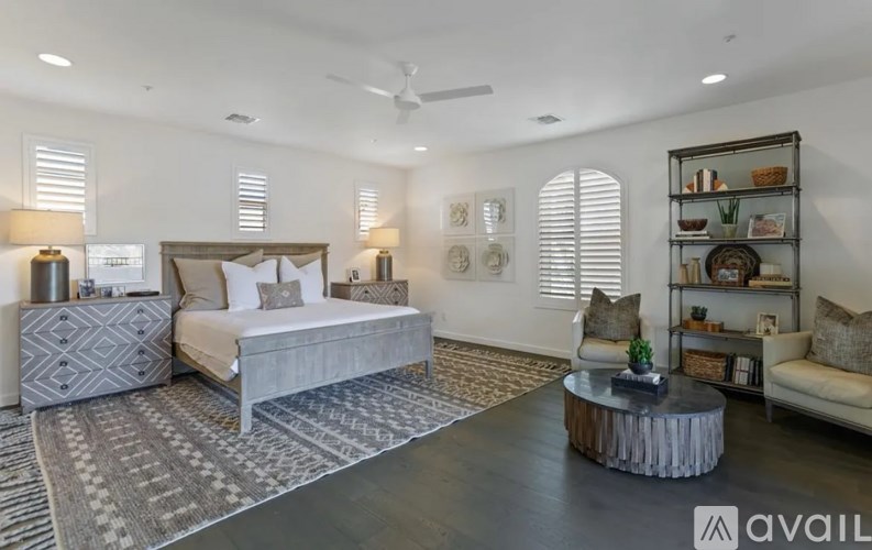 A well-lit bedroom with a large bed, a side table, and a shelf with decorative items.