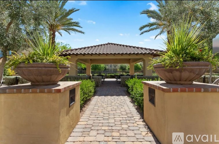 A garden with a brick pathway leading to a gazebo with two large planters on either side.