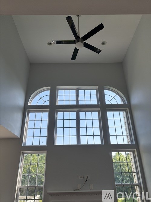 A room with a ceiling fan and large windows.