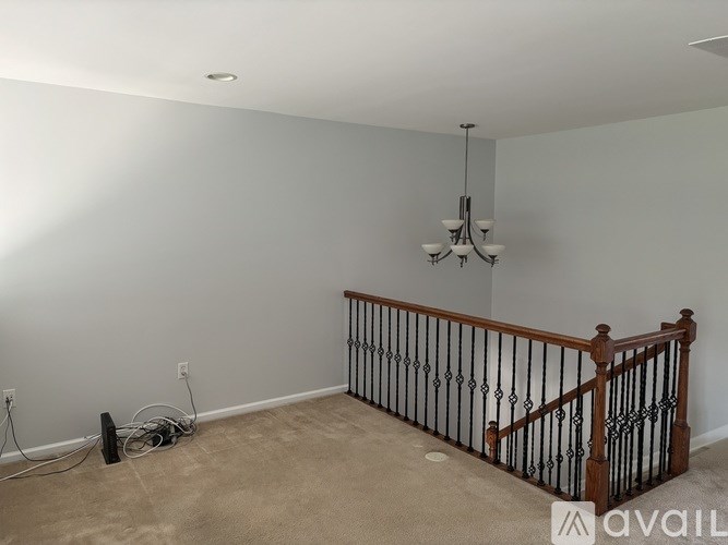 A room with a chandelier, a wooden railing, and a beige carpet.