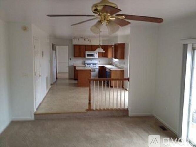 A living room with a ceiling fan and a kitchen area in the background.