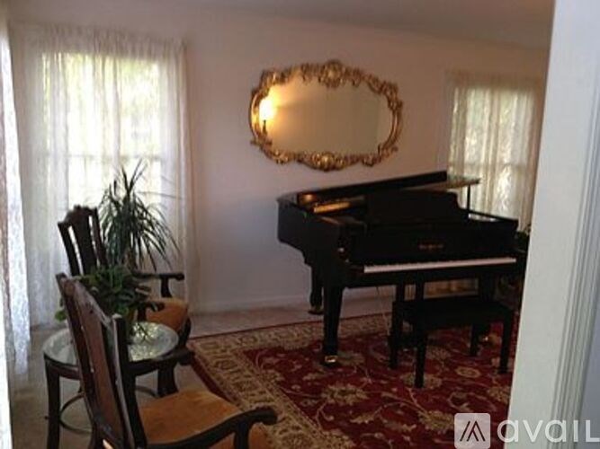 A grand piano sits in a living room with a mirror and a potted plant.