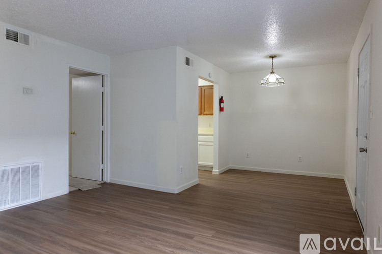 A room with wooden floors and white walls, with a door on the left and a fire extinguisher on the wall.
