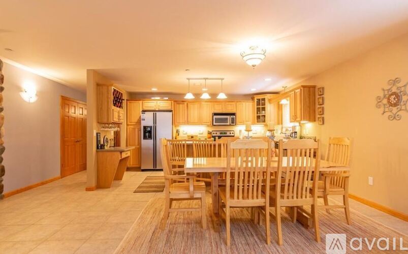 A dining room with a table set for six and a kitchen area with a refrigerator, microwave, and oven.