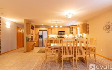 A dining room with a table set for six and a kitchen area with a refrigerator, microwave, and oven.