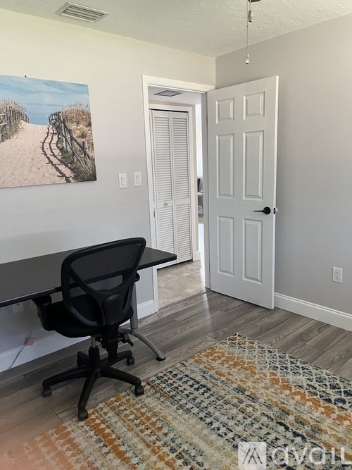 A room with a black chair and a painting of a beach scene on the wall.